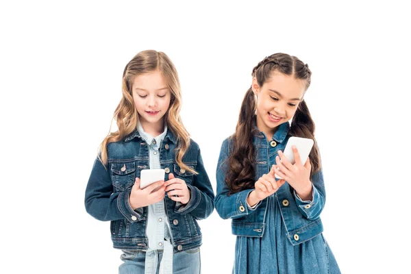 Dos niños en ropa de mezclilla usando teléfonos inteligentes aislados en blanco - foto de stock