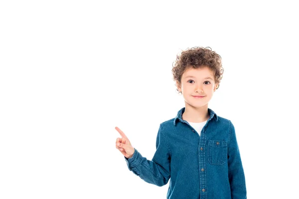 Vista frontale del bambino sorridente in camicia di jeans che punta con il dito isolato sul bianco — Foto stock