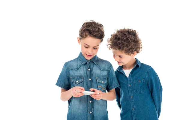 Dos niños en camisas de mezclilla usando teléfono inteligente aislado en blanco - foto de stock