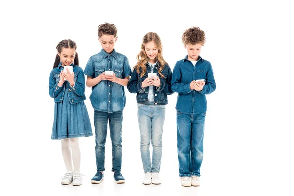 Vue pleine longueur de quatre enfants en vêtements en denim à l'aide de smartphones isolés sur blanc — Photo de stock