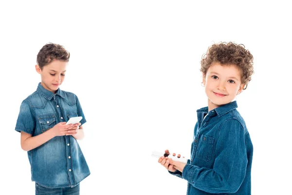 Duas crianças em camisas jeans usando smartphones isolados em branco — Fotografia de Stock