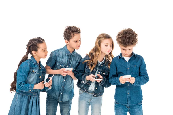 Четыре ребенка в джинсовой одежде с помощью смартфонов, изолированных на белом — стоковое фото