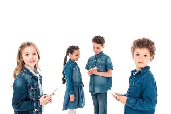 Four kids in denim clothes using smartphones isolated on white — Stock Photo