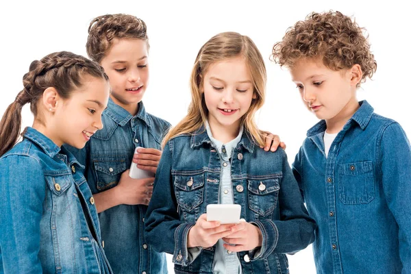 Четыре ребенка в джинсовой одежде с помощью смартфонов, изолированных на белом — стоковое фото