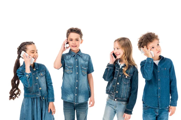 Quatro crianças em roupas jeans falando em smartphones isolados em branco — Fotografia de Stock