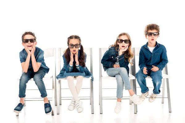 Cuatro niños sorprendidos en gafas 3D sentados en sillas en blanco - foto de stock