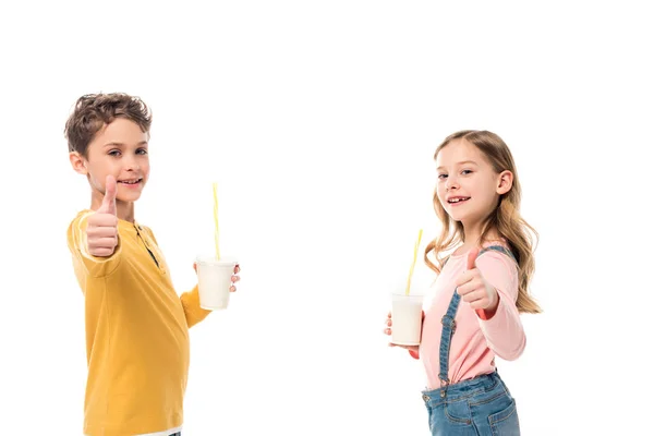 Two kids holding milkshakes and showing thumbs up isolated on white — Stock Photo