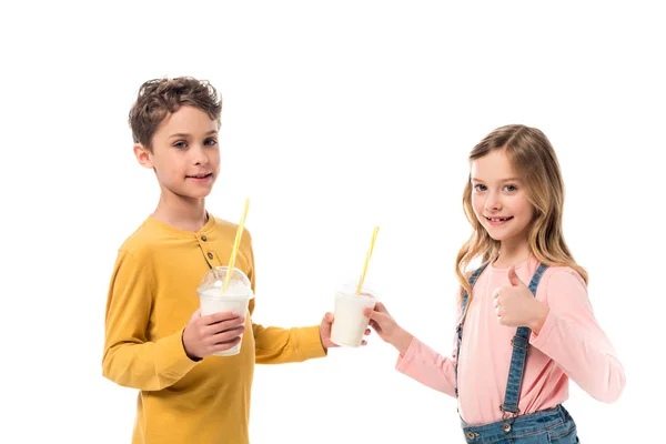 Duas crianças segurando milkshakes e mostrando polegar para cima isolado no branco — Fotografia de Stock
