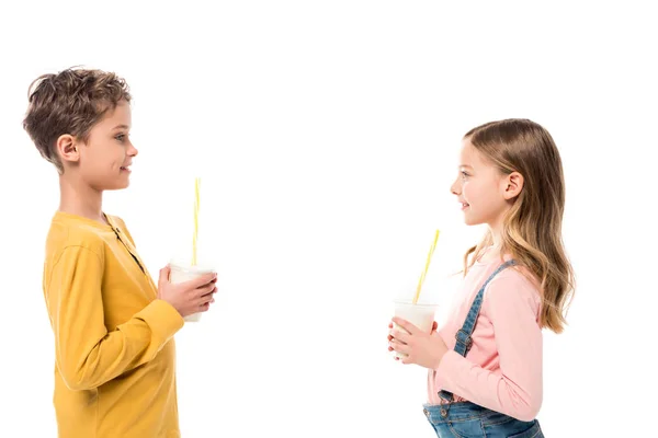 Вид збоку на двох дітей, що тримають молочні коктейлі і дивляться один на одного ізольовані на білому — стокове фото
