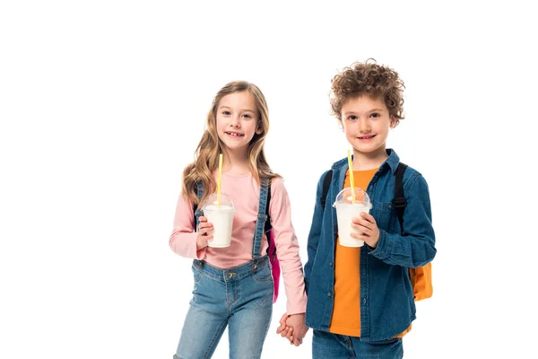 Schoolkids with backpacks and milkshakes holding hands isolated on white — Stock Photo