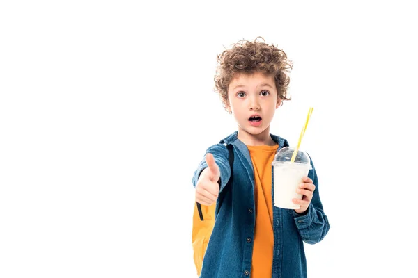 Shocked schoolkid holding milkshake and showing thumb up isolated on white — Stock Photo