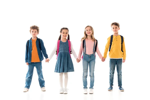 Vista completa de los escolares con mochilas cogidas de la mano aisladas en blanco - foto de stock