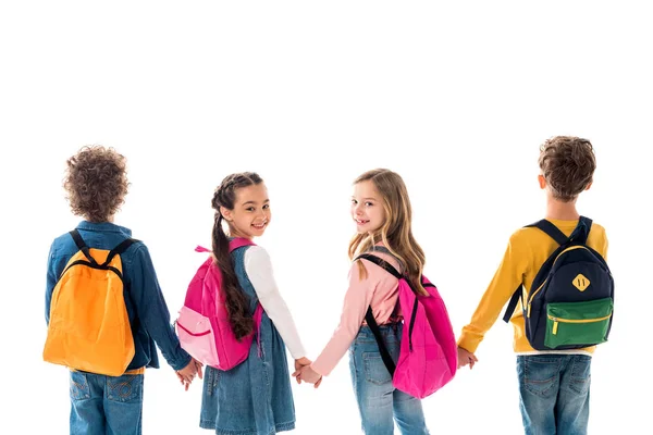 Schulkinder mit Rucksäcken, die sich an den Händen halten und isoliert auf Weiß zurückblicken — Stockfoto