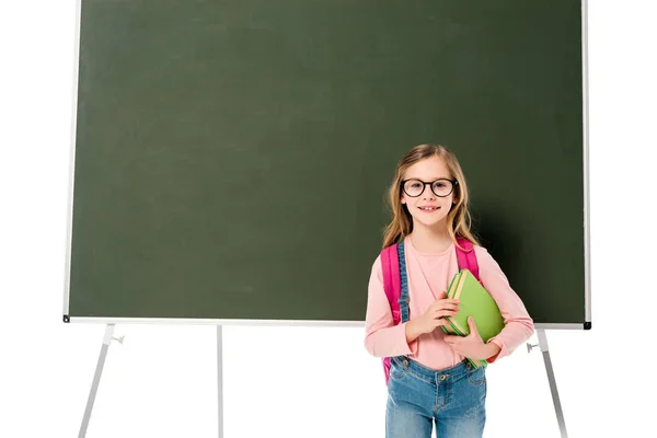 Front view of schoolgirl with backpack and books standing near blackboard isolated on white — Stock Photo