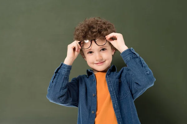 Sonriente niño rizado con gafas mirando a la cámara aislada en verde - foto de stock