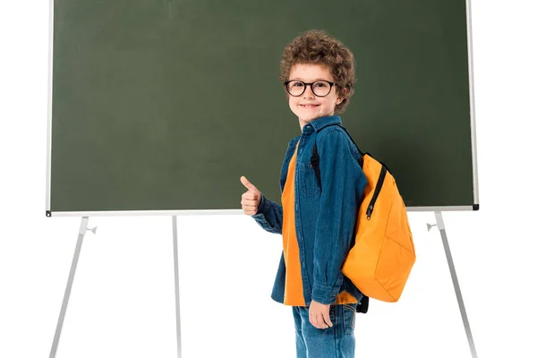 Écolier souriant dans des lunettes debout près du tableau noir et montrant pouce vers le haut isolé sur blanc — Photo de stock