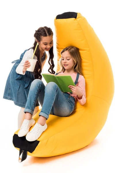 Deux enfants souriants avec haricot sac chaise livre de lecture sur blanc — Photo de stock