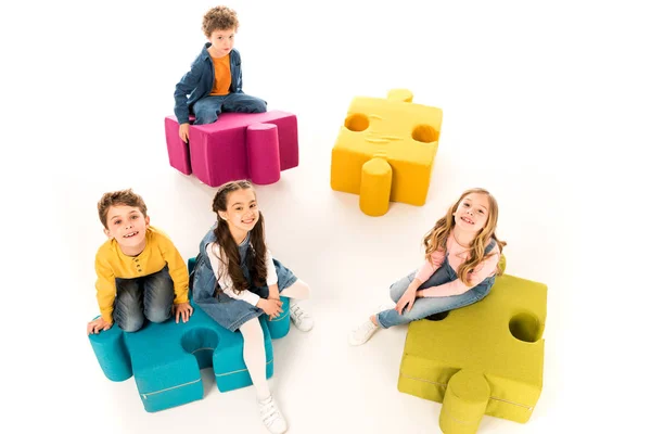 Overhead view of kids sitting on jigsaw puzzles on white — Stock Photo