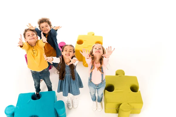 Overhead view of kids with outstretched hands near colorful jigsaw puzzles on white — Stock Photo