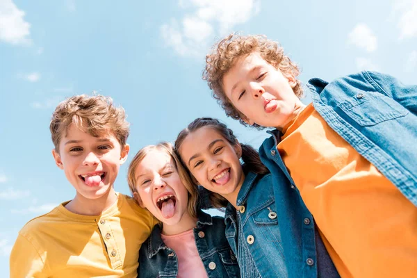 Низький кут зору чотирьох дітей, що показують язики під небом — стокове фото