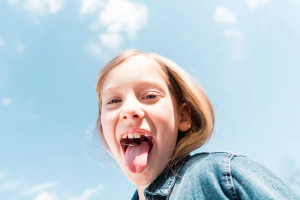 Low angle view of happy kid showing tongue under sky — Stock Photo