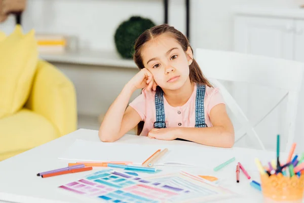 Selektiver Fokus eines aufgebrachten Kindes, das mit Zeichnung auf eine Kamera in der Nähe von Papieren blickt — Stockfoto