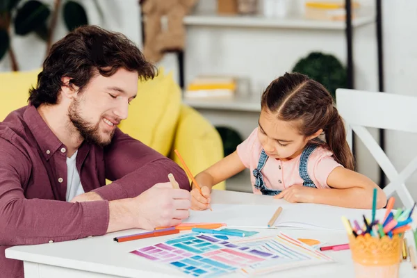 Padre allegro disegno su carta vicino figlia carina a casa — Foto stock