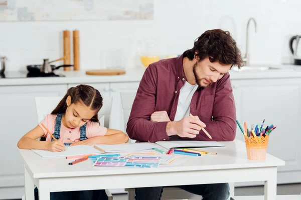 Красивый отец и милая дочь рисуют на бумагах дома — стоковое фото