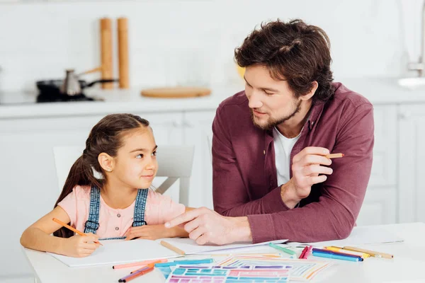 Cute daughter looking at handsome father pointing with finger at paper — Stock Photo