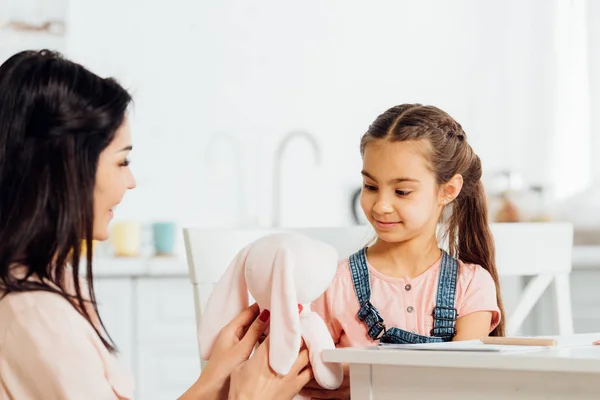 Selective focus of happy kid looking at soft toy in hands of mother — Stock Photo