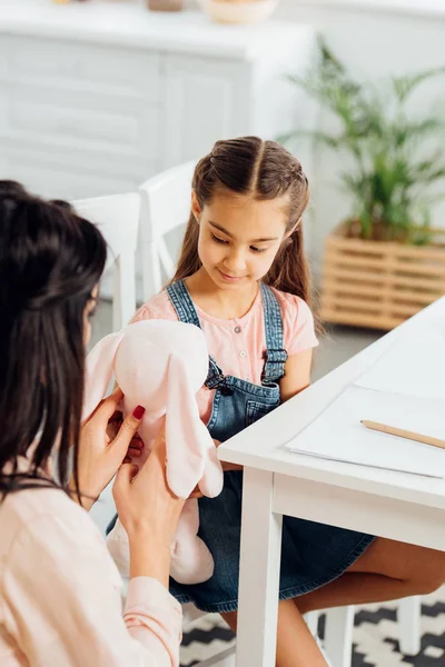 Selective focus of happy kid looking at soft toy in hands of brunette mother — Stock Photo