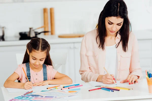 Attractive brunette mother and cute daughter drawing at home — Stock Photo