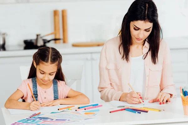 Atractiva morena madre y linda hija dibujo en casa - foto de stock