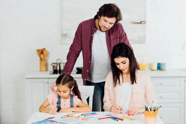 Bello padre in piedi e guardando bruna moglie e figlia disegno a casa — Foto stock