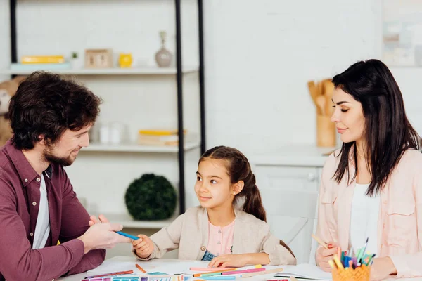 Happy father giving felt pen to cute daughter near attractive wife — Stock Photo