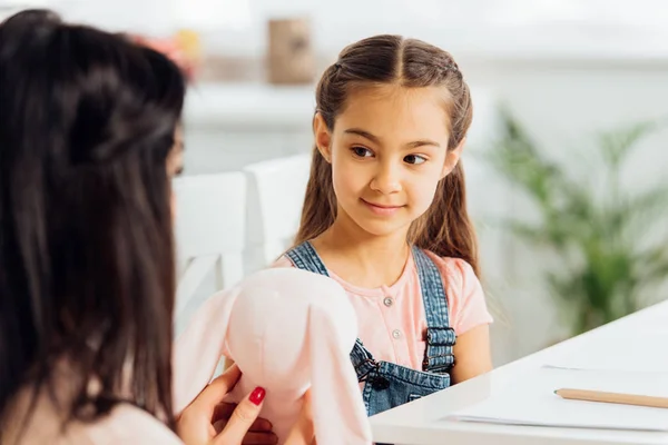 Messa a fuoco selettiva della figlia carina guardando la madre che tiene in mano il giocattolo morbido — Foto stock