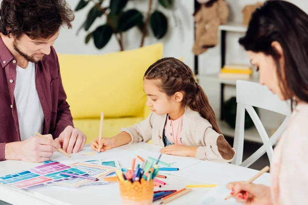 Enfoque selectivo de linda hija y padre dibujo cerca de la madre morena - foto de stock