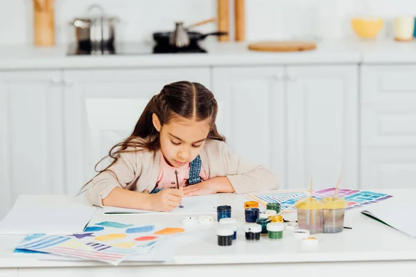 Concentrado y lindo niño pintura en papel en casa - foto de stock