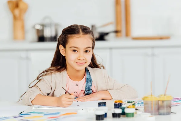 Cheerful kid looking at camera and holding paintbrush at home — Stock Photo