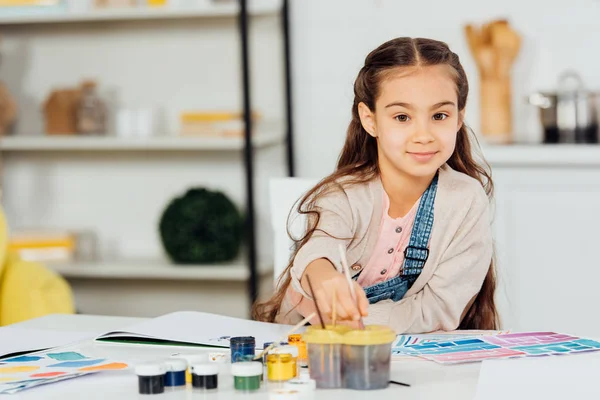 Cheerful kid looking at camera while holding paintbrush at home — Stock Photo