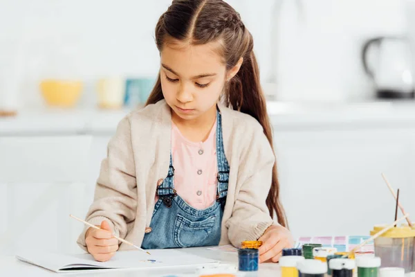 Konzentriertes Kinderzeichnen mit Pinsel auf Papier zu Hause — Stockfoto