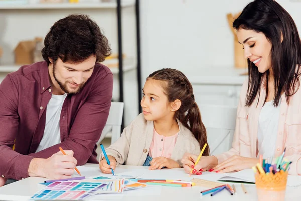 Criança alegre olhando para o pai desenho com lápis de cor em casa — Fotografia de Stock
