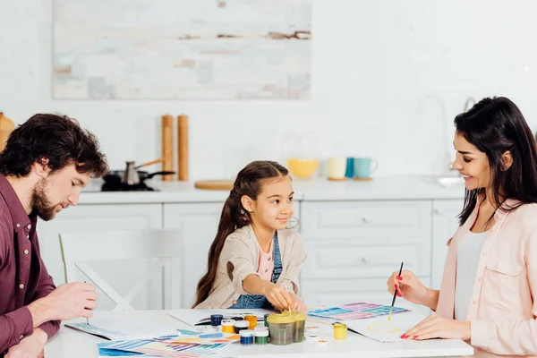 Lindo niño mirando a madre mientras padre dibujo en papel - foto de stock