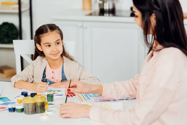 Selektiver Fokus des glücklichen Kindes, das auf die Mutter mit dem Pinsel blickt — Stockfoto