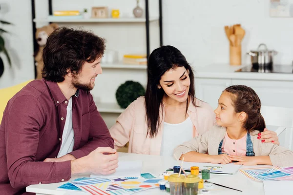 Feliz madre abrazando alegre hija cerca de marido en casa - foto de stock