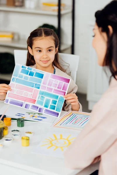 Enfoque selectivo de lindo niño sosteniendo papel con rayas de colores cerca de la madre - foto de stock