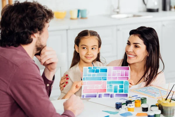 Foyer sélectif de mignon enfant tenant du papier avec des rayures colorées près de la mère et le père — Photo de stock
