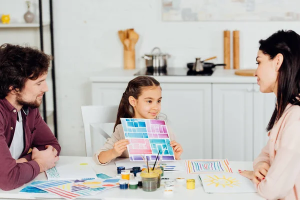 Niño alegre sosteniendo papel con rayas de colores cerca de los padres en casa - foto de stock
