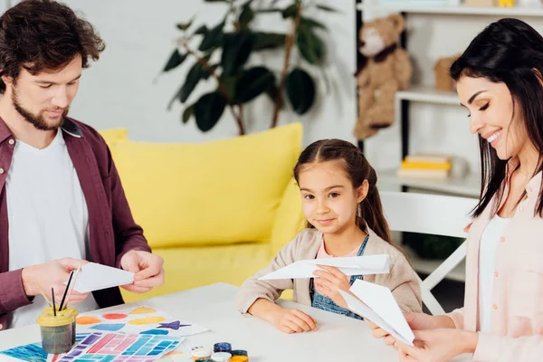 Happy parents and cute daughter holding paper planes at home — Stock Photo