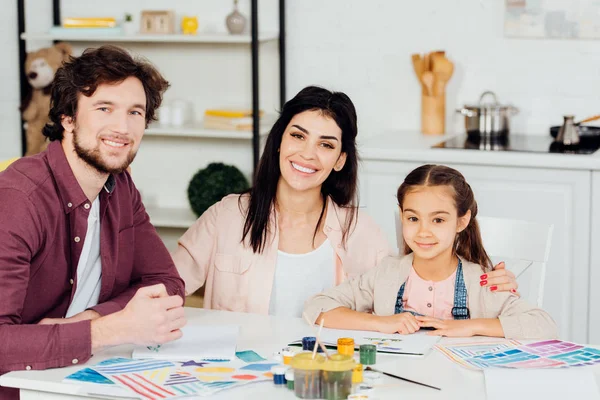 Familia alegre mirando a la cámara y sonriendo cerca de papeles con dibujo en casa - foto de stock